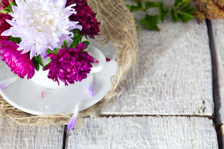 Pink flowers in a decorative cup on white rustic vintage backgroundの写真素材