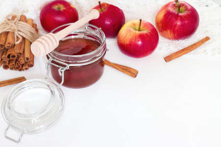 Honey in glass jar and apple with cinnamon sticks on white backgroundの写真素材