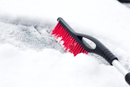 Transportation, winter, weather, people and vehicle concept - man cleaning snow from car with brush