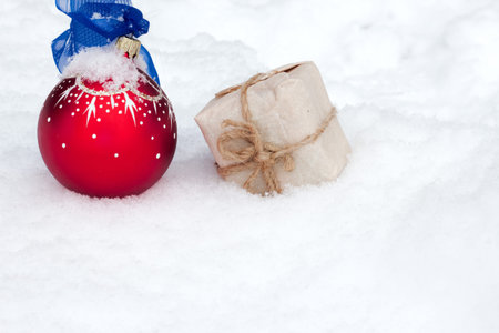 Red christmas ball and gift in craft paper on snow. Christmas background