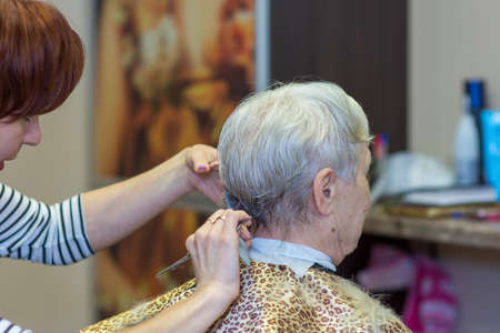 Chelyabinsk, Russia, March 18, 2019. Haircut for the elderly. The process of cutting in the hair salon. Senior woman getting her hair curled at a beauty salon.のeditorial素材