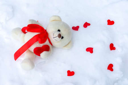 A toy bear with hearts lies on the ground against a snowdrift. Sad Valentine's day card designの写真素材