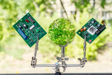 The microprocessors are fixed with a magnifying glass and robot hands against a background of green trees. Concept of the impact of e-waste on the environment and nature.の写真素材
