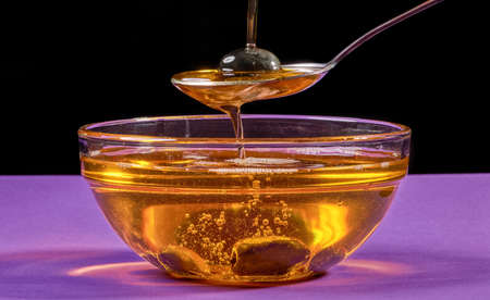 Olive oil is poured from a spoon into a bowl. photo on a lilac backgroundの写真素材