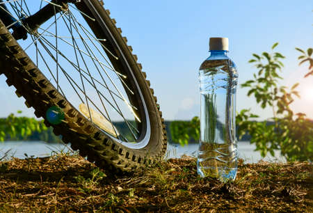 A bottle of clean water and a Bicycle wheel on the background of the lake shore. Rest after exercise on a summer evening.の写真素材