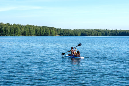 Young women swim together on a SUP Board in the calm Bay of the lake. July 12, 2020 Lake Uvildy, Ural, Russiaの写真素材