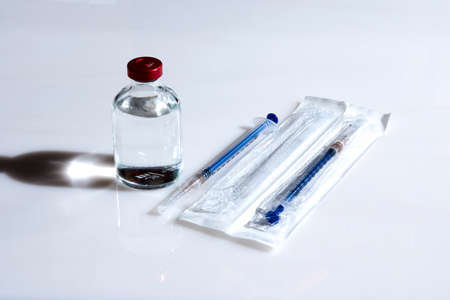 A bubble with a clear liquid and two syringes on a light background. The concept of a vaccine to protect against infection.の写真素材