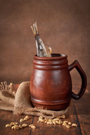 Beer clay brown mug with beer and dried fish on a wooden table on a dark background.
