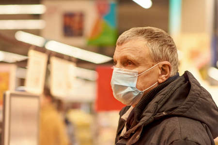 A 65-year-old man in a blue medical mask picks up groceries at a supermarket. Buying food during the coronavirus pandemic.の写真素材