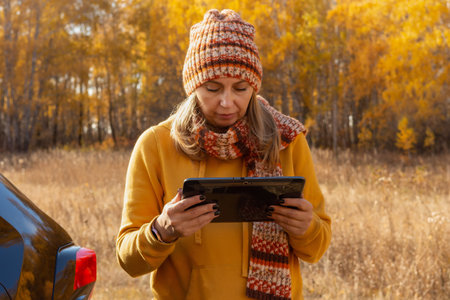 A woman uses a tablet on a car trip on vacation in the fall. A woman reads a guidebook map on a...