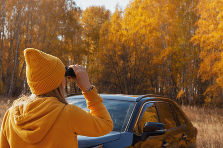 A beautiful positive woman in yellow clothes with binoculars at a picnic on an autumn day. The concept of the road, freedom, rest, travelの写真素材