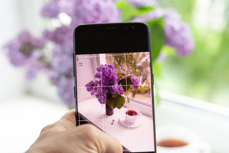 woman photographs a lilac flower arrangement on window on a smartphone for social networks