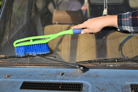 A hand using a green and blue cleaning brush on a car windshieldの写真素材