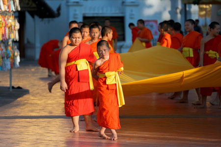 Nan, Thailand - December 1, 2019: Young monks hold a huge orange canvas at Wat Phrathat Chae Haeng....