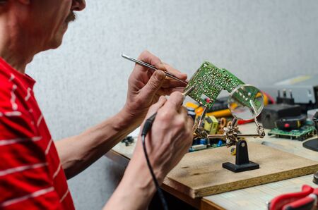 Electronic technician repairs mobile phone using soldering iron, tweezers and magnefierの写真素材