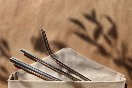 Reusable stainless steel straws in textile bag on kraft background, hard light. Zero waste, no plastic concept. Metal tool for eco friendly lifestyle. Horizontal brown banner with copy space, flat layの写真素材
