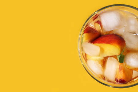Peach cocktail with ice on bright yellow background. Horizontal banner, poster with copy space for advertising summer holiday, sales. Cold drink with mint, pieces of fruit in glass. Flat layの写真素材