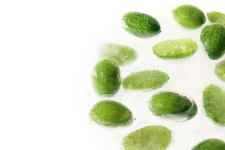 Close up of frozen cucamelon in ice, white background. Horizontal poster, banner, copy space. Concept of shock freezing of food. Preservation of summer vitamins. Group of small green exotic fruitsの写真素材
