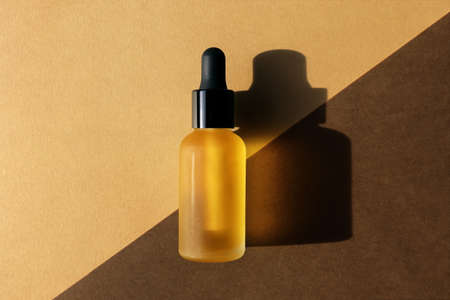 Dropper oil bottle on diagonal background, flat lay. Monochrome brown mockup, banner, poster. Natural cosmetic, eco lotion, essence, serum, emulsion. Body care concept. Hard light, central compositionの写真素材