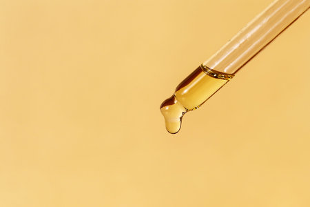 Pipette with falling drop of oil. Dropper with lotion, essence, serum, emulsion. Horizontal monochrome banner, poster, copy space, beige yellow background. Natural organic cosmetic. Body care conceptの写真素材