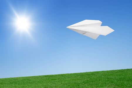 Paper airplane flying over the lawn against the blue skyの写真素材