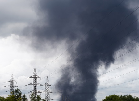 black smoke over an industrial area and high voltage power linesの写真素材