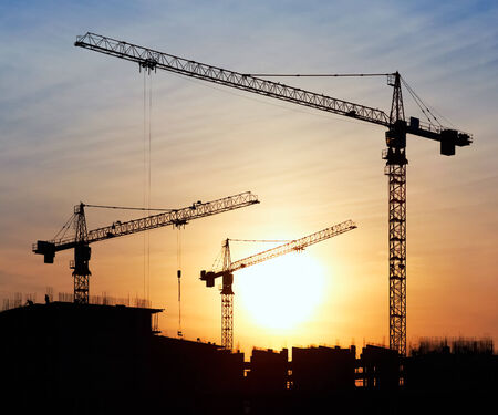 Silhouettes of construction cranes against the evening skyの写真素材