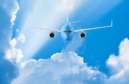 Airplane flying in the blue sky among clouds and sunlightの写真素材