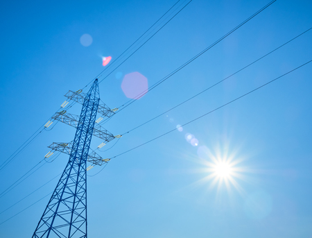 High voltage power lines on the background of blue sky with the sunの写真素材