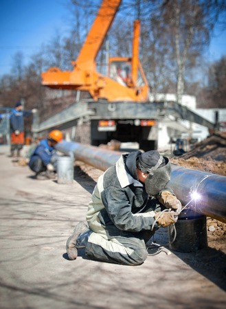 Welder welding pipe on background of the construction siteの写真素材