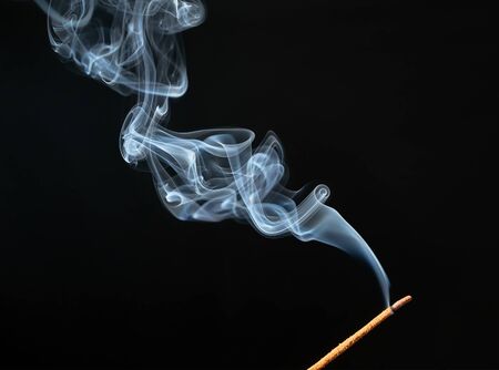 Burning incense stick with smoke on black background.の写真素材