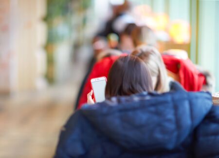 Smartphone in a woman's hand, blurred or defocus image of restaurant or cafeteria for use as background.の写真素材