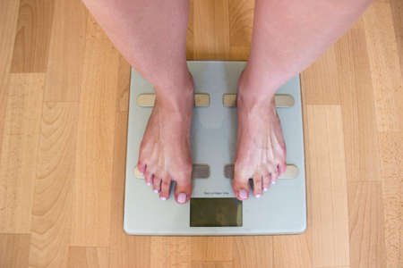 Beautiful female legs stand on the scales. Gray scales stand on the floor while a person is weighed on them.の写真素材