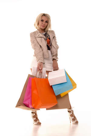 Beautiful blonde stands on a white background with purchases in her hands. The girl raised her leg and is glad that she bought so many things.の写真素材