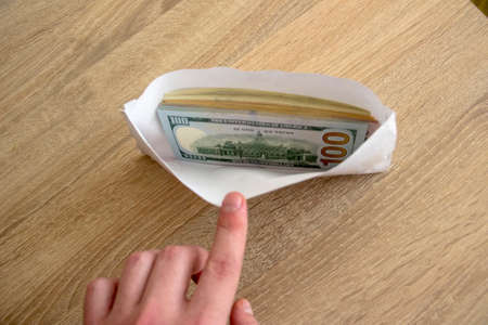 Man hand shows an envelope with money. Money dollars lie in a white envelope for an employee. The employee salary lies in an envelope.の写真素材