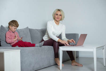 Mom works at the laptop while her son plays phone.の写真素材