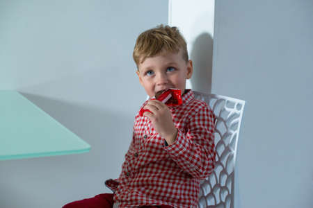 Boy sits on the kitchen and eats chocolate bar.の写真素材