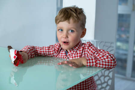 Boy eats a chocolate bar while sitting in kitchen.の写真素材