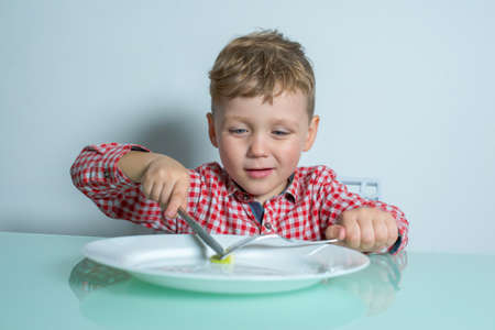 Little boy cuts a vegetable on a plate with knife.の写真素材