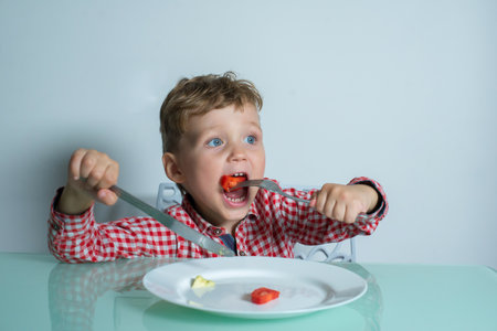 Boy eats food in the kitchen at the table.の写真素材