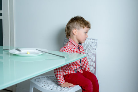 Boy sits in the kitchen and refuses to eat.の写真素材