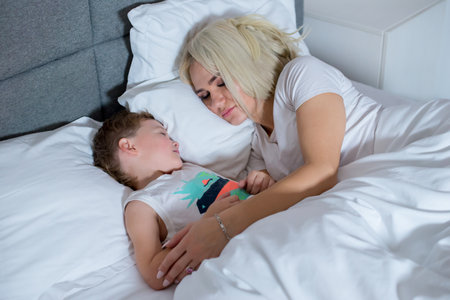 Mom sleeps with little son in bed at home.の写真素材