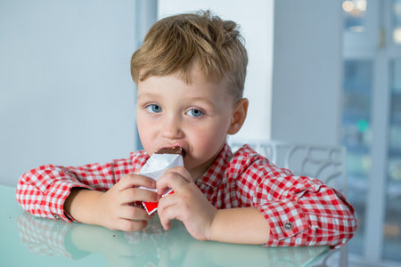 Boy eating delicious chocolate bar in kitchenの写真素材
