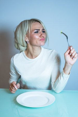 Sick girl sits at the table and eats a vegetable.の写真素材