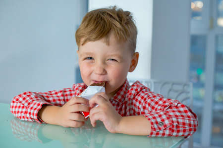 Little boy eating delicious chocolate in kitchen.の写真素材