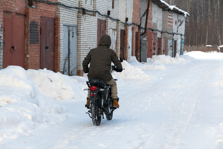 a man in winter clothes riding a motorcycle on a snowy roadの写真素材