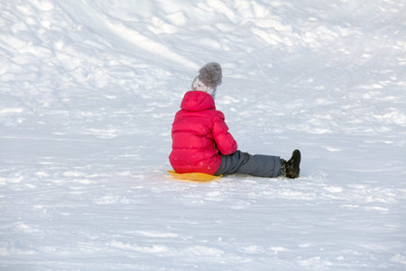 a 6 year old girl in a red winter jacket and winter pants sits on the snow