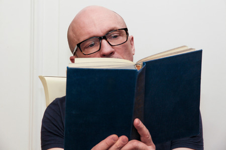 adult bald man in glasses reading a bookの写真素材