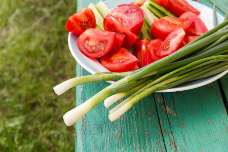 green onions, tomatoes and cucumbers in a plate on a wooden tableの写真素材