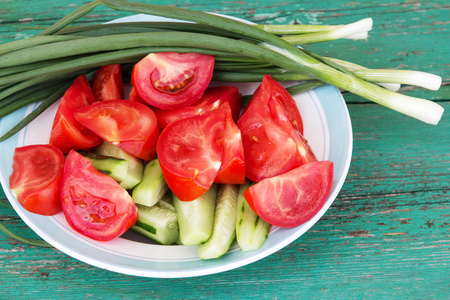 green onions, tomatoes and cucumbers in a plate on a wooden tableの写真素材